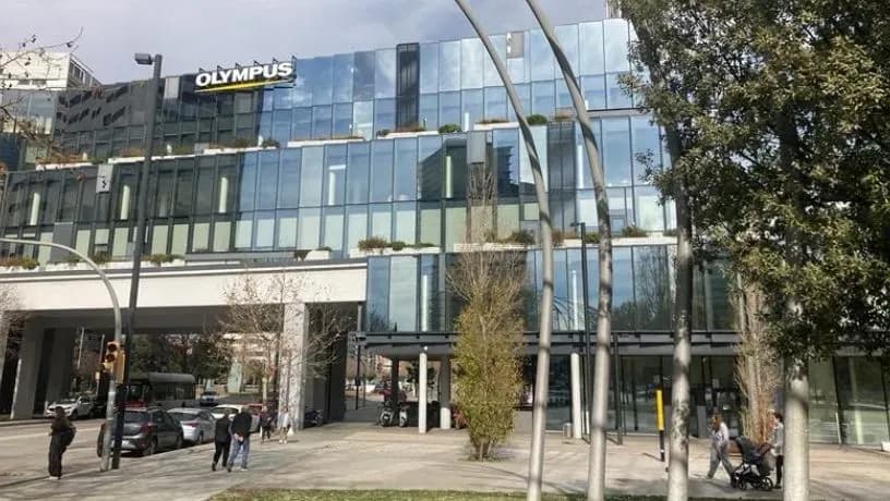 Exterior view of Olympus headquarters with glass facade, balconies, and visible company logo.