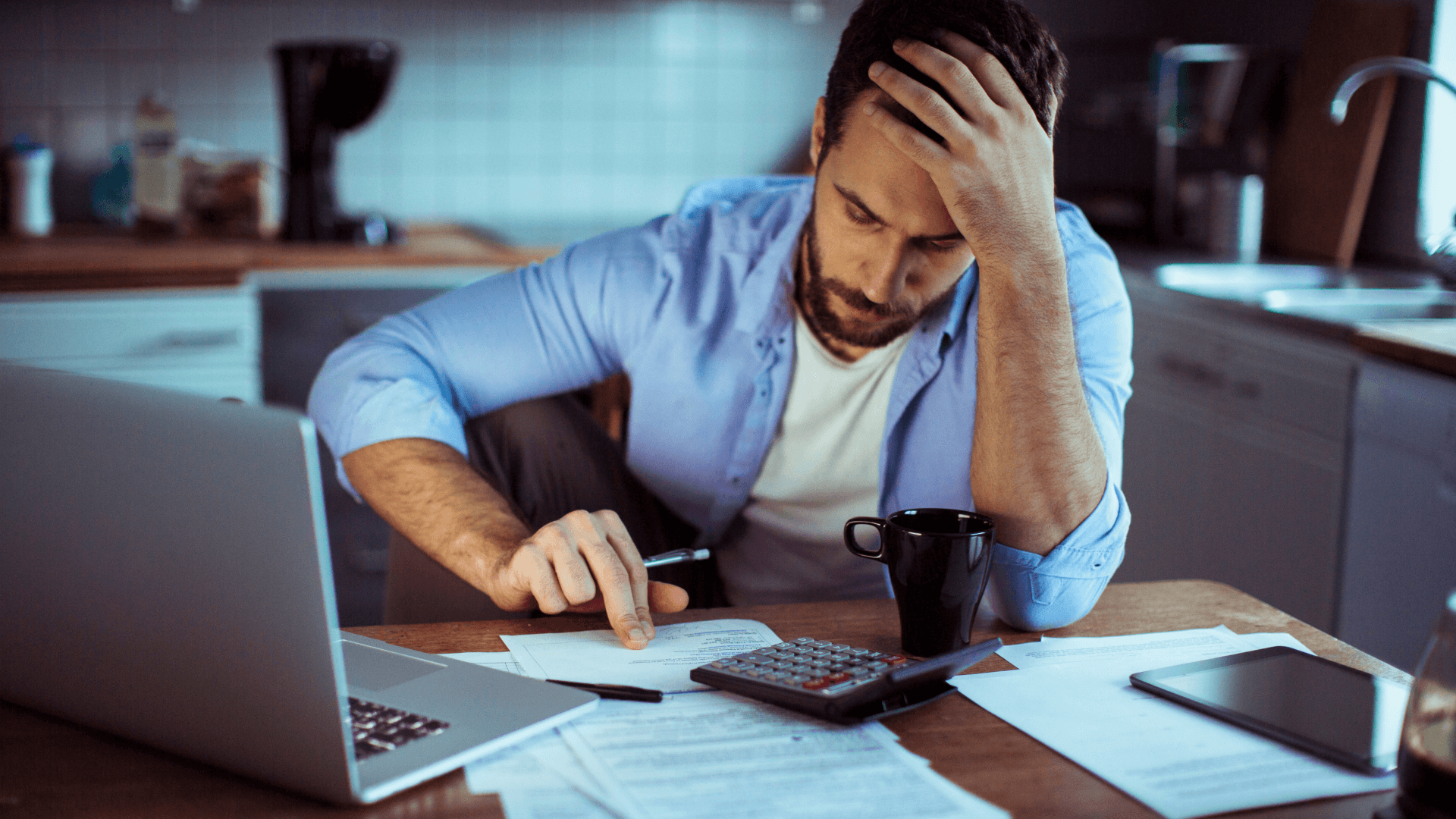 Person reviewing invoices manually with documents, laptop, calculator, and coffee on the table.