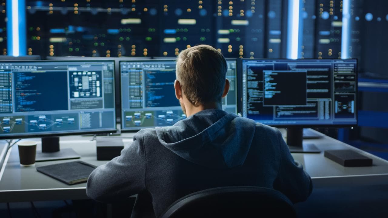 Person at a desk with multiple monitors displaying data and code, representing data monitoring for a DDM strategy.