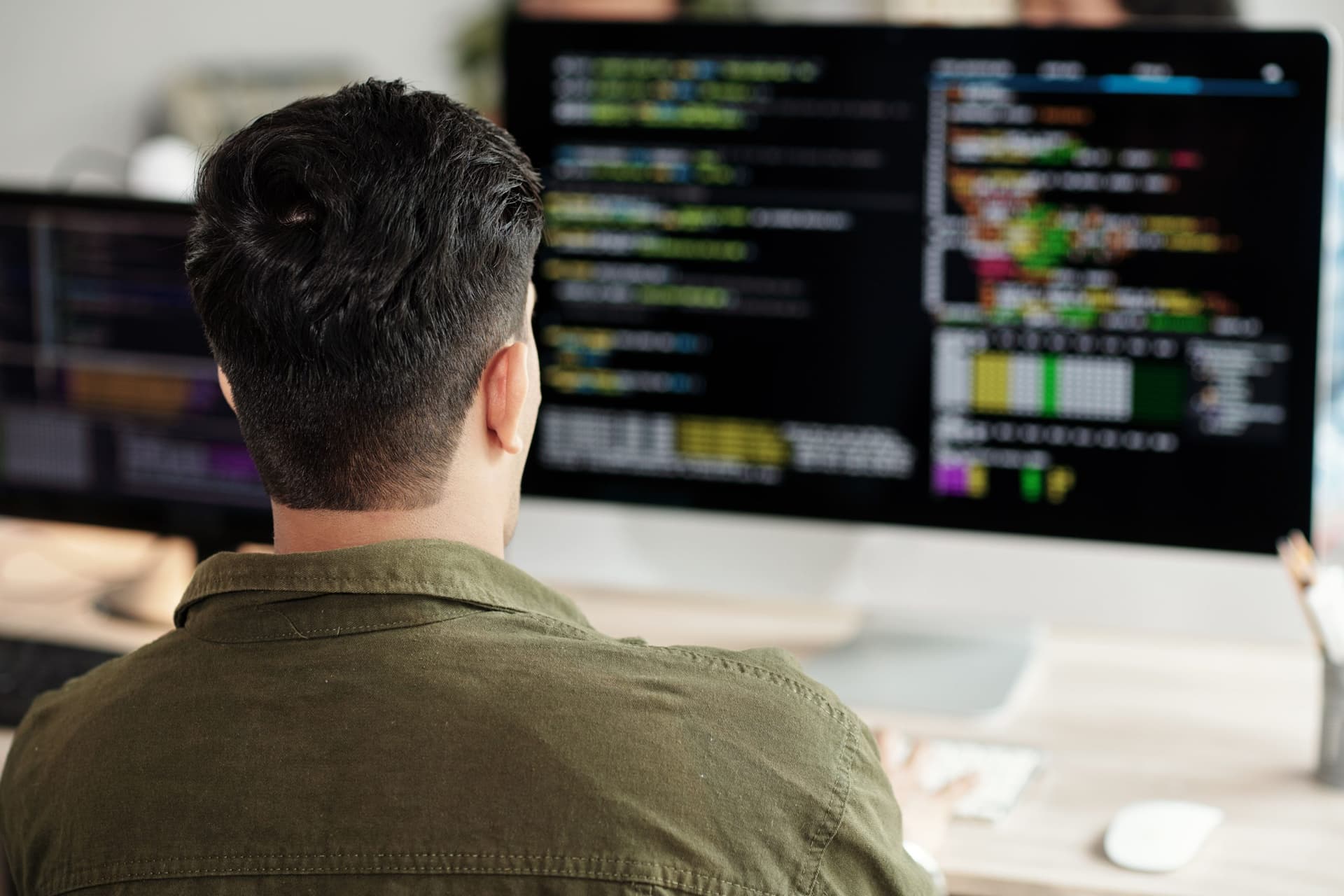 Person working at a desk with two monitors displaying code, representing technical configuration of Azure Front Door services.