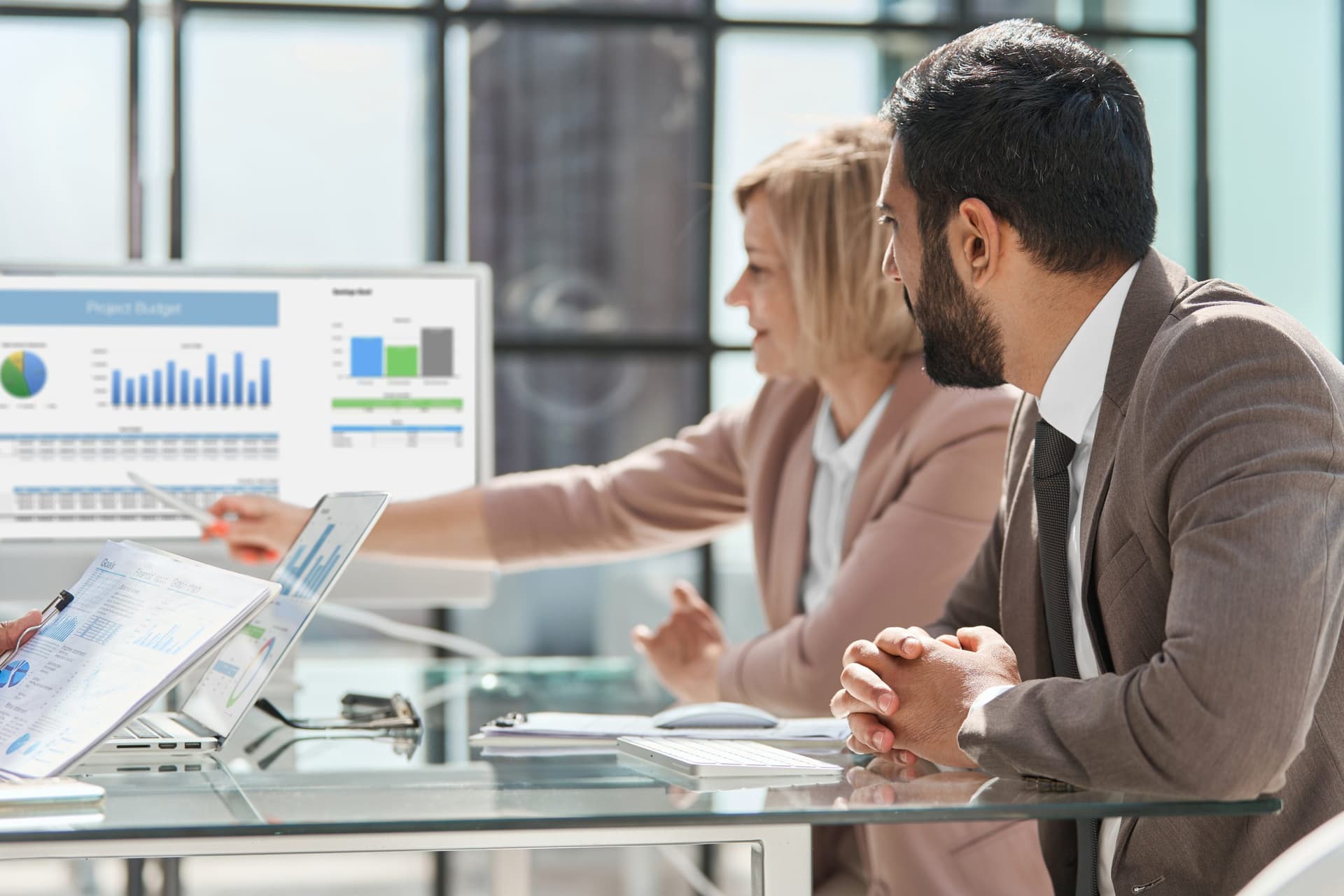 Two professionals reviewing charts and graphs on a computer screen at a glass table, representing business analytics and decision-making with Microsoft Dynamics 365.