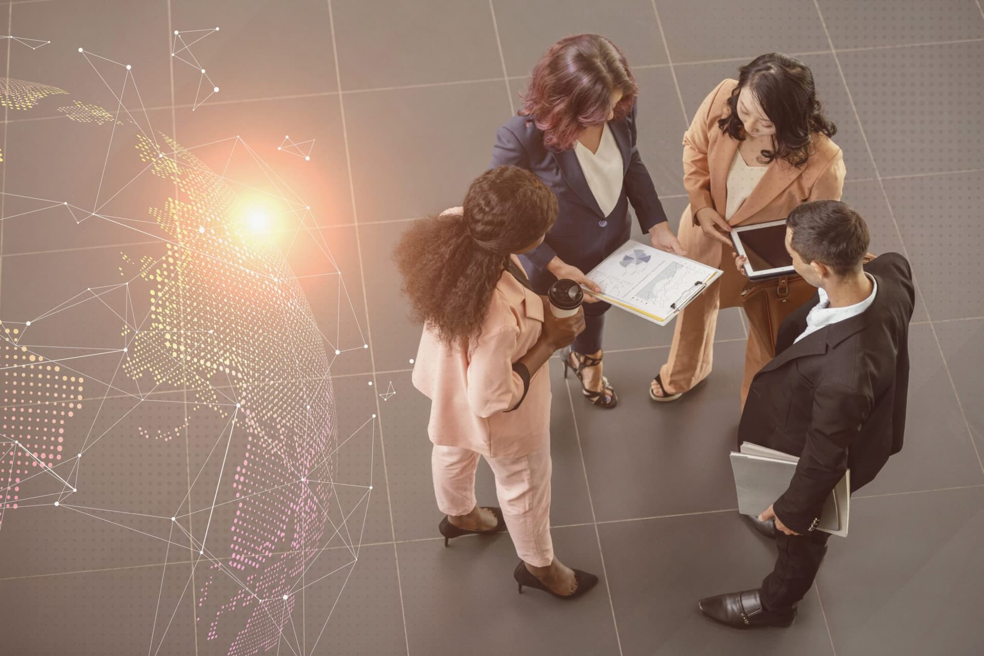 Top view of four professionals collaborating, one holding a clipboard and another using a tablet.