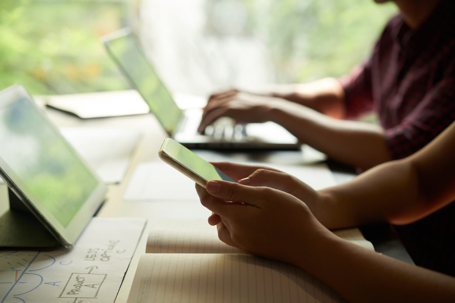 Two professionals working on laptops, one holding a smartphone, representing multi-device corporate environments.