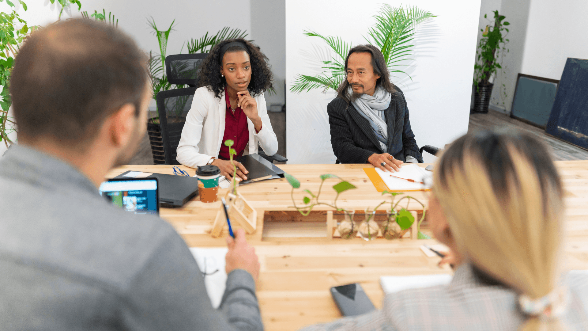 Four people sitting around a table in an office, engaged in discussion, representing collaborative work using SharePoint.