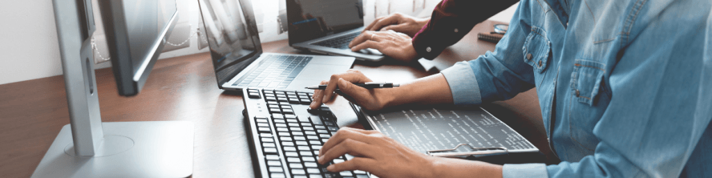 Office environment with people working on laptops and monitors, representing the implementation of cybersecurity protocols in daily operations.