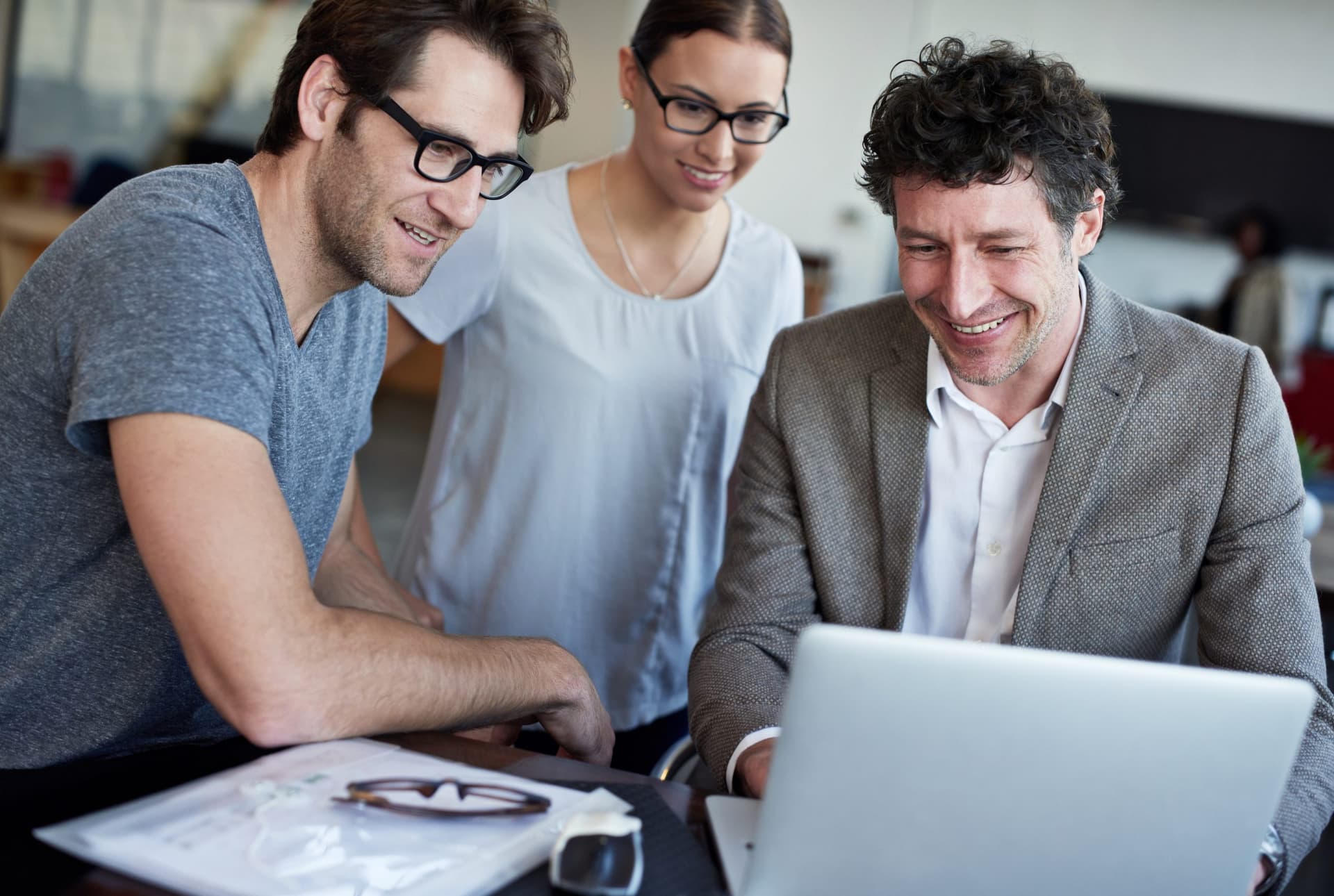 Three people collaborating around a laptop, representing teamwork and professional engagement in modern web and e-commerce development.