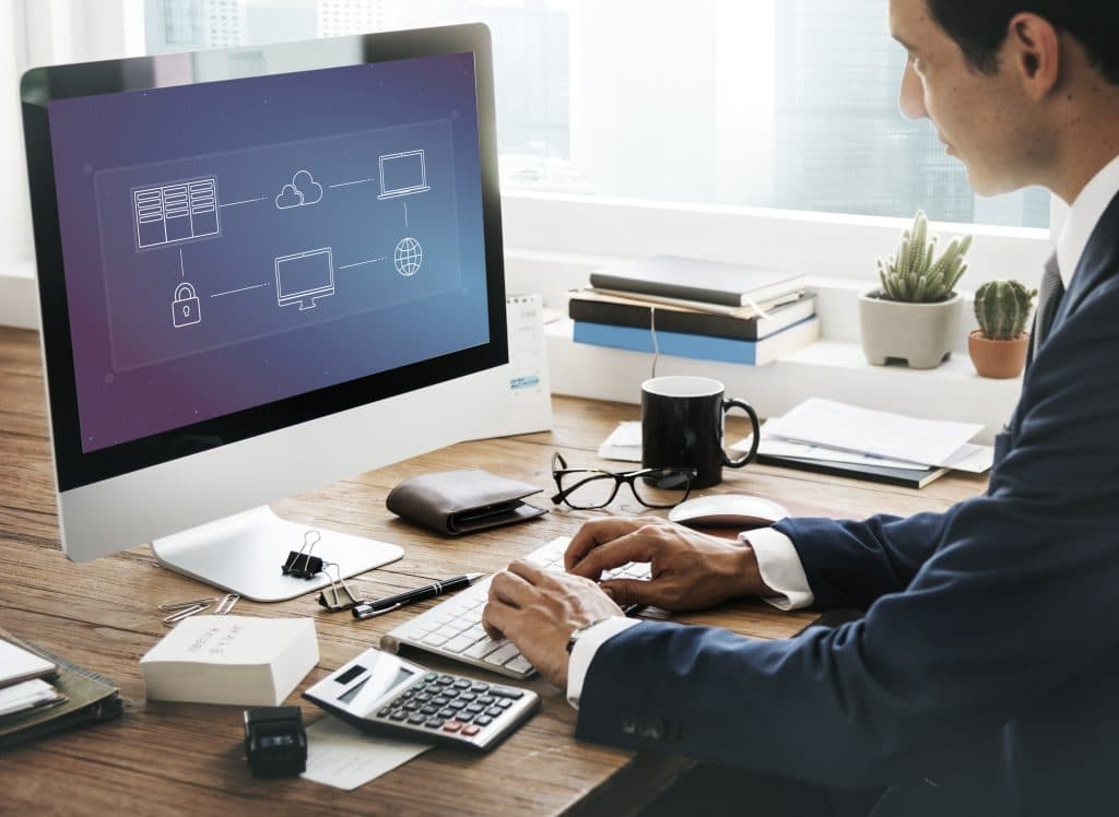 Individual at desk viewing computer screen with network diagrams of servers and cloud services, representing IT infrastructure management.